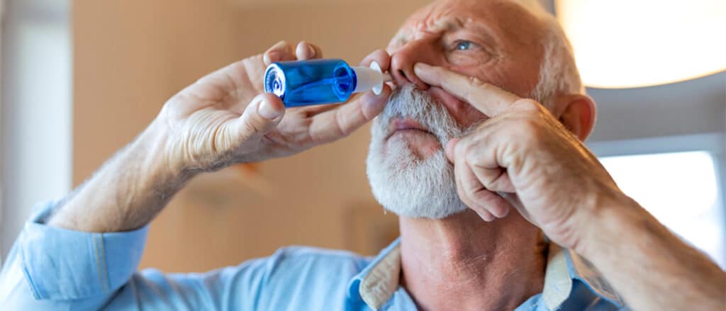 Een oude man die één neusgat gesloten houdt terwijl hij een zoutoplossing in zijn neus sprayt.