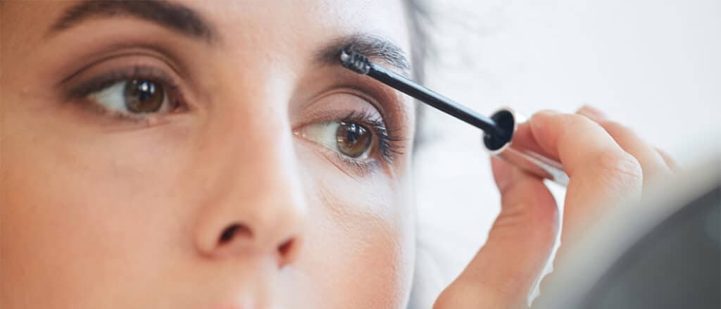 Close up van een vrouw met bruine ogen die wenkbrauw gel aanbrengt op haar wenkbrauwen.